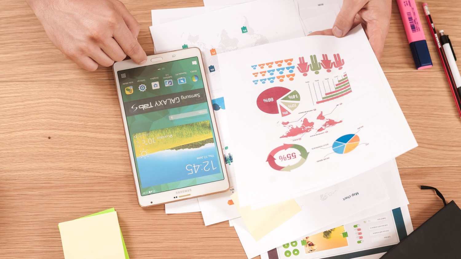 Die 5 besten Infografik Tools: Person überprüft Infografiken mit einem Samsung Tablet und gedruckten Diagrammen auf einem Schreibtisch