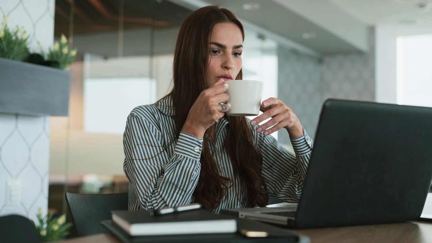 Frau trinkt Kaffee und arbeitet am Laptop.