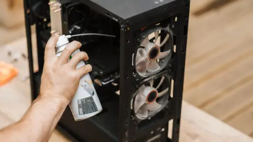 Person reinigt das Innere eines Computergehäuses mit Druckluft