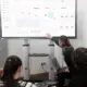 Group of professionals engaged in a business presentation examining charts on a large screen.