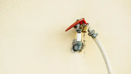 Nahaufnahme eines Außenwasserhahns mit rotem Drehgriff an einer Wand