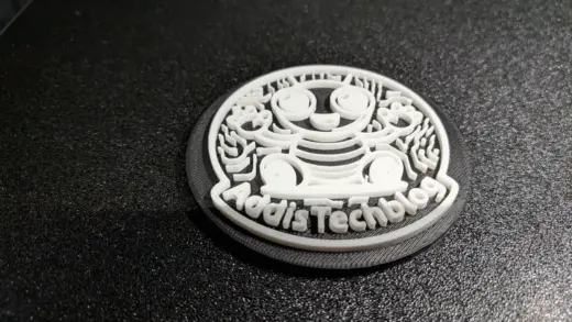 Nahaufnahme eines zweifarbig gedruckten Logo-Untersetzers auf der texturierten Druckplatte, die unteren Schichten sind am Rand sichtbar