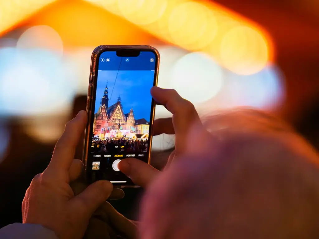 Hände halten ein Smartphone und fotografieren eine beleuchtete Szene bei Nacht