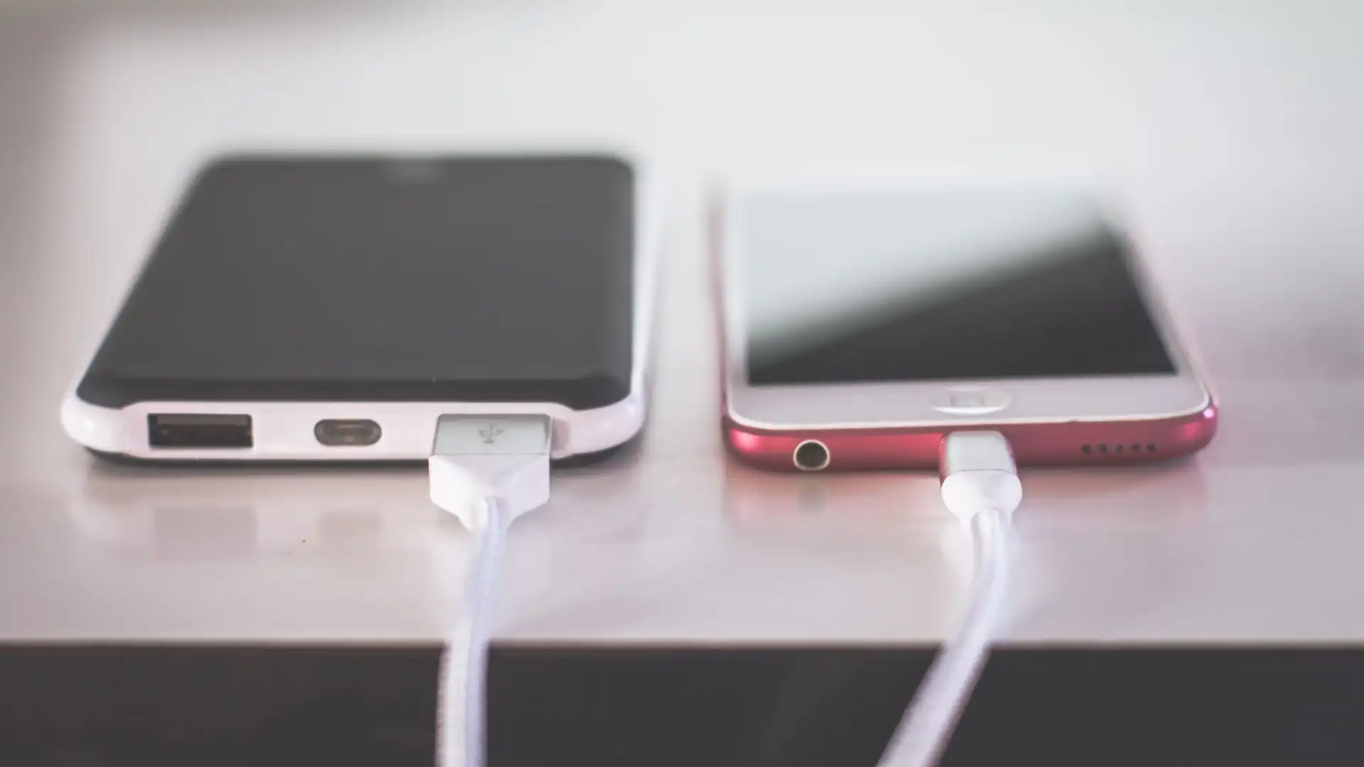 Zwei Smartphones liegen nebeneinander auf einem Tisch und laden per Kabel