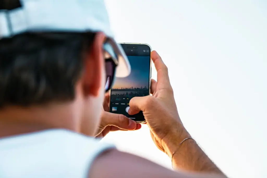 Person fotografiert eine Stadtsilhouette bei Sonnenuntergang mit dem Smartphone
