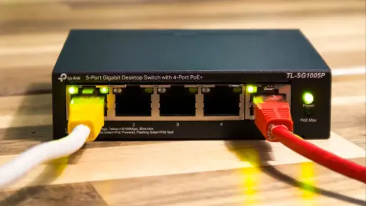 Netzwerk-Switch mit mehreren eingesteckten LAN-Kabeln auf einer Holzoberfläche
