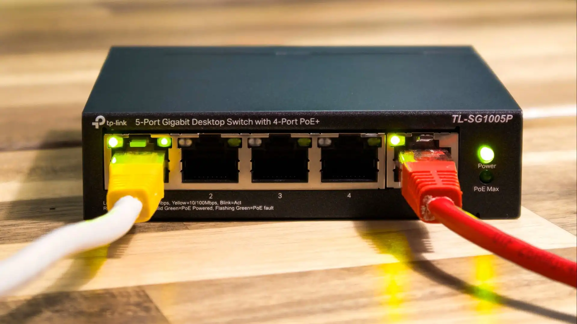 Netzwerk-Switch mit mehreren eingesteckten LAN-Kabeln auf einer Holzoberfläche