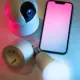 Smarte Kamera und smarte Glühbirne neben einem Smartphone als Steuerzentrale