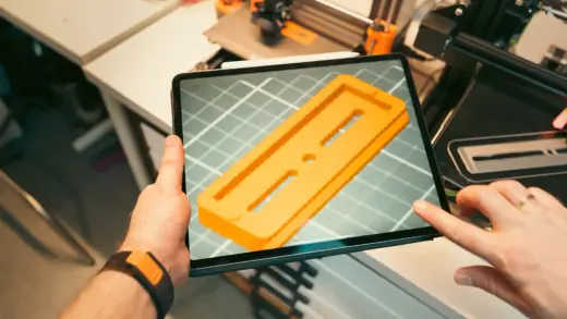Person prüft ein 3D-Modell auf einem Tablet in einer Werkstatt mit 3D-Druckern