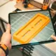 Person prüft ein 3D-Modell auf einem Tablet in einer Werkstatt mit 3D-Druckern