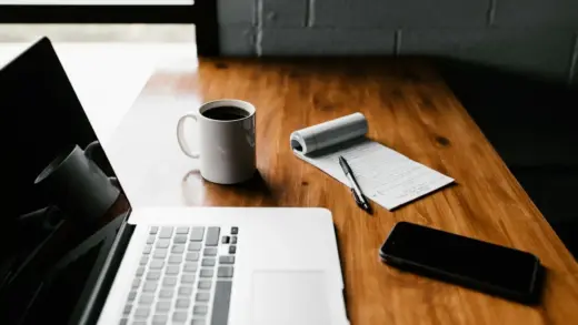 Aufgeräumter Schreibtisch am Morgen mit Laptop, Kaffeetasse und Notizbuch