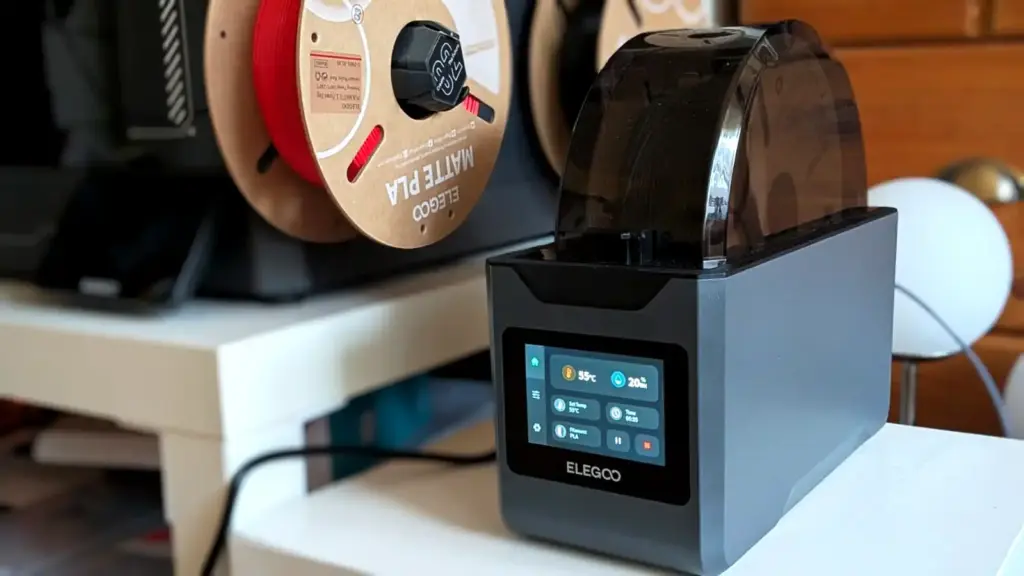 Elegoo H1 HT Filamenttrockner trocknet PLA bei 55 °C, im Hintergrund offen hängende Filamentspulen