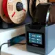 Elegoo H1 HT Filamenttrockner trocknet PLA bei 55 °C, im Hintergrund offen hängende Filamentspulen