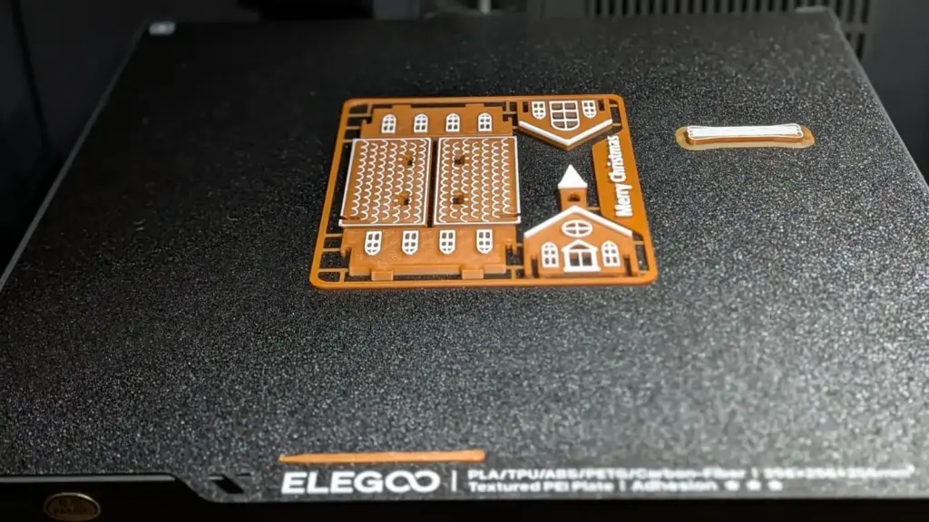 Zweifarbig gedruckte Kit Card einer Lebkuchenkirche mit Merry-Christmas-Schriftzug auf der texturierten PEI-Platte des Elegoo Centauri Carbon 2