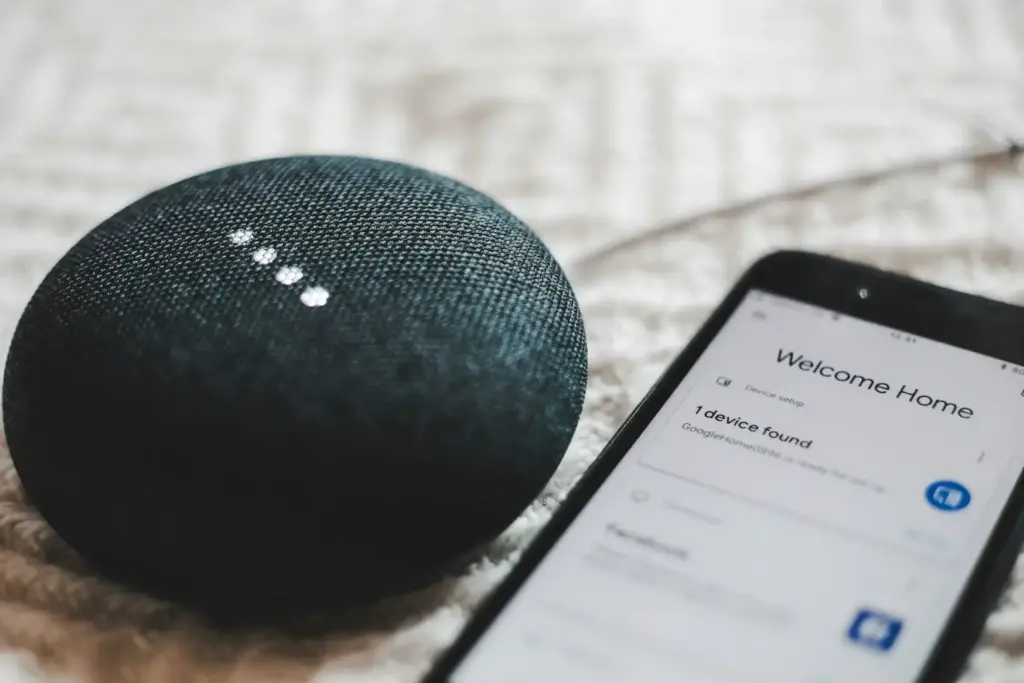 Smarter Lautsprecher mit Smartphone daneben auf einer Ablage